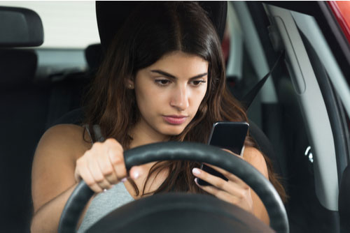 Young woman looking at her mobile phone while driving