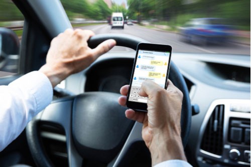 Close-up Of A Man's Hand Typing Text Message on Mobile Phone While Driving A Car